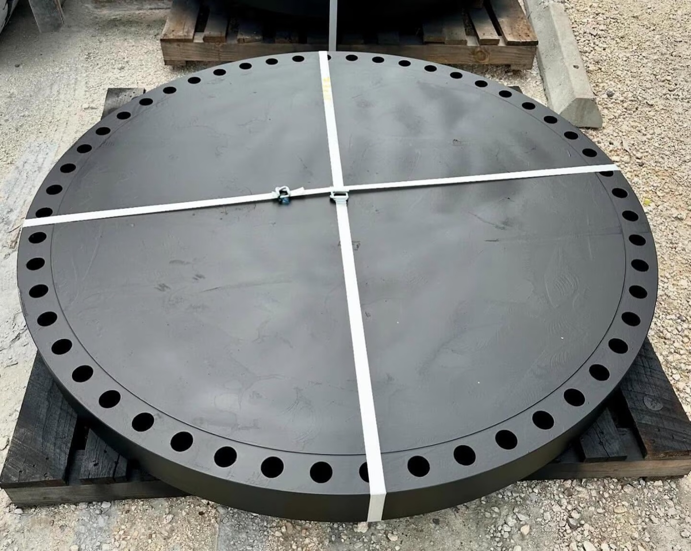 Large diameter ASTM A105 carbon steel blind flange black coated and strapped on wooden pallet in the yard