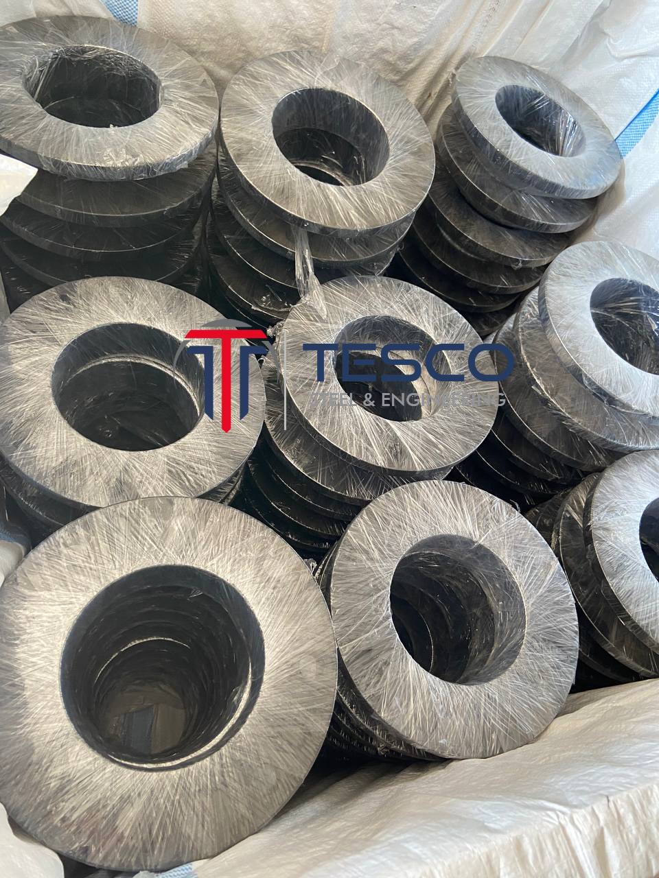Close-up of ASTM A350 LF2 LTCS weld neck flanges individually plastic-wrapped showing bore detail — low temperature carbon steel flanges export packaging Tesco Steel India