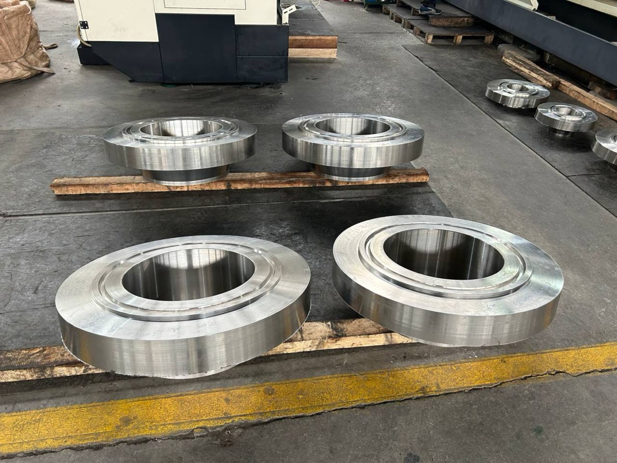 Machined RTJ flanges with ring grooves stacked on wooden battens beside the CNC machining centre