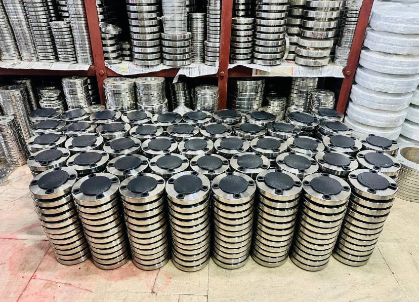 Large bulk stock of stainless steel blind flanges with face-protection plastic caps stacked before dispatch — Tesco Steel & Engineering Mumbai